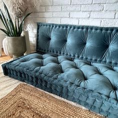 a blue velvet couch sitting on top of a rug next to a potted plant