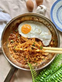 two eggs are on top of noodles in a pan with chopsticks next to them