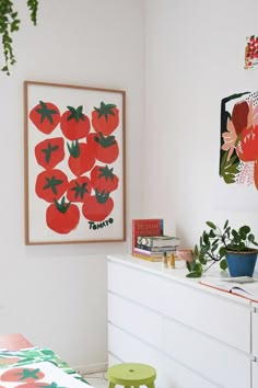 a bedroom with white walls and lots of artwork on the wall, including red tomatoes