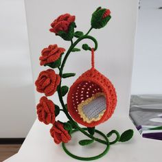 a crocheted vase with red flowers and green stems on a white table top