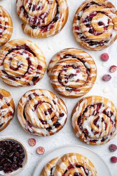 cranberry cinnamon rolls with white icing and cherries on a plate next to other pastries