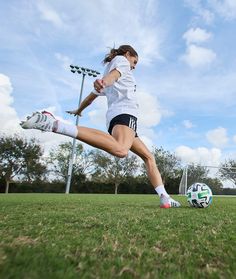 a woman kicking a soccer ball on top of a field