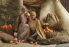 two women sitting on the ground surrounded by oranges