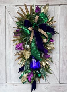 a wreath with purple, green and gold decorations hanging on a white wooden wall next to a door