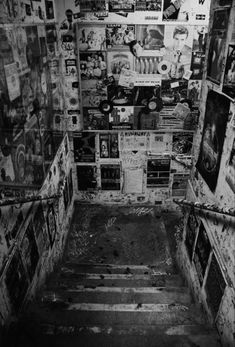 black and white photograph of an abandoned building with posters on the walls, stairs leading up to the second floor