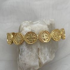 Gorgeously unique, this stunning medal coin cuff bracelet is perfect for wearing alone or stack with some of our gold fill bead bracelets. The Benedictine Medal is one of the most powerful symbols of divine protection. Wear this petite bracelet as a reminder that you are protected by God's army and as St Benedict did, to do good every day.  Tradition holds that it stands for the power of prayer in times of temptation and suffering, wards against evil, and symbolizes how prayer creates peace within ourselves and in our communities. Specifications - Adjustable cuff, one size fits most, up to wrist size 7.5 18kt gold plated or sterling silver plated God's Army, Czech Beads Jewelry, Catholic Bracelet, Powerful Symbols, Petite Necklace, The Power Of Prayer, Divine Protection, Dainty Gold Bracelet, Coin Bracelet