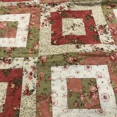 an old quilt is laying on top of a tablecloth with red and green flowers