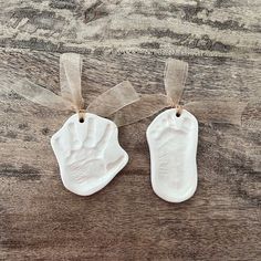 two white ceramic handprints hanging from twine on wooden table with clear ribbon