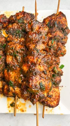 chicken skewers with sauce and herbs on a white plate