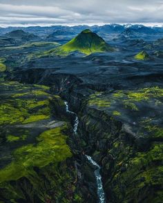 an aerial view of a river running through a valley with green mountains in the background