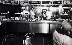 black and white photograph of three men in a restaurant kitchen with menus on the wall