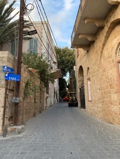 an alley way with stone buildings and palm trees on both sides, surrounded by cobblestone streets