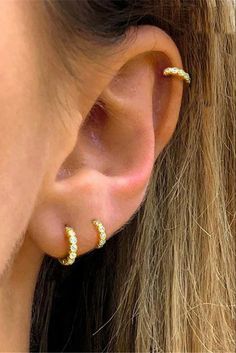 a woman wearing gold ear piercings with small white stones on the top of her ears