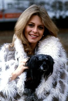 a woman holding a small dog in her arms and smiling at the camera while wearing a fur coat