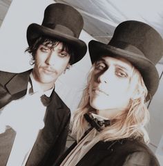 two people dressed in black hats and tuxedos