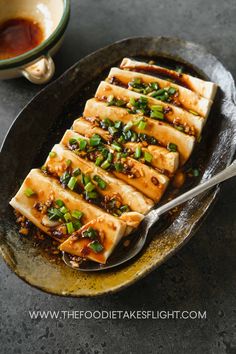 tofu with sesame seeds and green onions in a skillet next to a cup of sauce