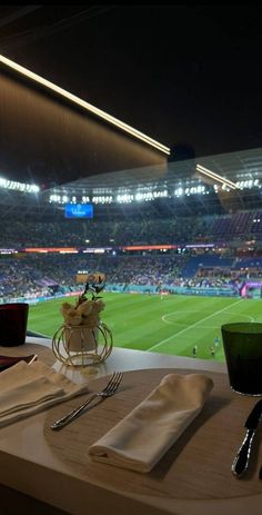 a table set with silverware and napkins in front of a view of a soccer stadium