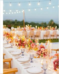 a long table is set up with flowers and candles for an outdoor wedding reception in the evening