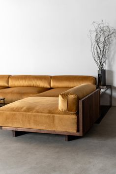 a brown couch sitting next to a wooden table on top of a cement floor in front of a white wall