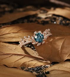 an engagement ring with blue topaz surrounded by leafy brown and green leaves on the ground