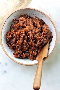 a wooden spoon in a bowl filled with meat and sauce on top of a marble counter