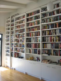 a room filled with lots of white bookshelves next to a door and windows