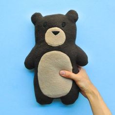 a hand is holding a black and white teddy bear on a blue background with one paw up to the camera