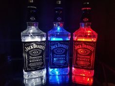 three bottles of jack daniels gin are lit up in the dark with colorful lights on them