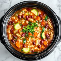 a crock pot filled with pasta, beans and cucumber garnish