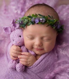 a baby is sleeping with a teddy bear wearing a wreath on it's head