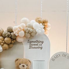 a teddy bear sitting in front of a bunch of balloons on the wall next to a sign that says something sweet is brewing