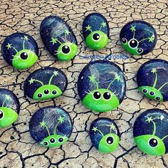 green and black painted rocks with eyes on them sitting in the middle of a cracked ground