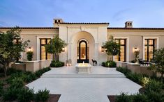 a large white house with lots of windows and plants on the front lawn at dusk