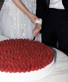 a bride and groom are cutting into a red velvet heart - shaped cake with white frosting