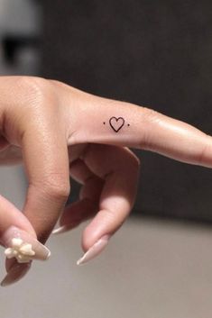 a woman's hand with a tiny heart tattoo on it, and the finger