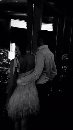 a man and woman standing next to each other in front of a window at night