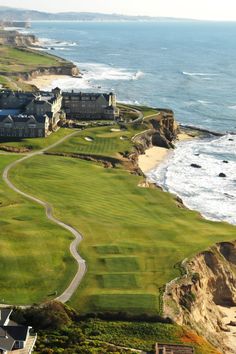 an aerial view of a golf course near the ocean with houses and cliffs in the background