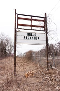 a black and white photo of a sign that says hello stranger in front of a fence