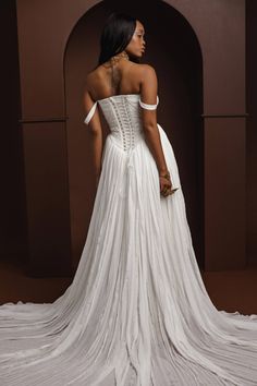 a woman in a white wedding dress standing on a brown floor with her back to the camera