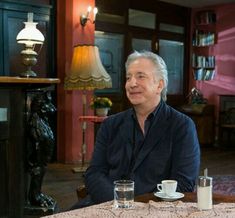 an older man sitting at a table with two cups and saucers in front of him