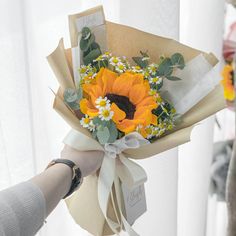 a bouquet of sunflowers is being held by someone's hand in front of a window