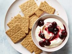 a white plate topped with crackers next to a bowl of ice cream and cherries