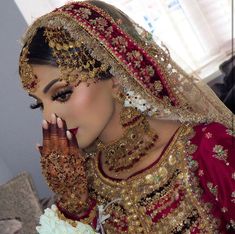 a woman in a red and gold bridal outfit holding her hands to her face