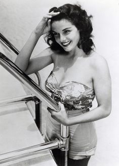 a black and white photo of a woman in a bathing suit on the stairs smiling