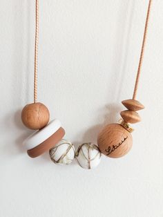 three necklaces hanging on a white wall, one is made from wood and the other has marble beads