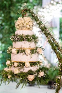 a three tiered wedding cake with white flowers and greenery hanging from the top