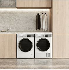 a washer and dryer sitting in a kitchen next to each other with clothes hanging on the wall