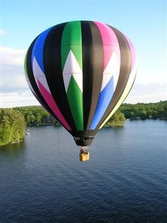 a colorful hot air balloon flying over a body of water with trees in the background