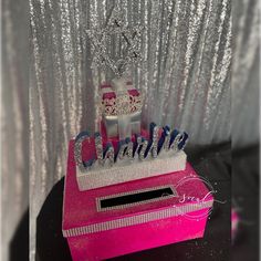 a pink box with silver glitter and a tiara on top that says charlotte in blue letters