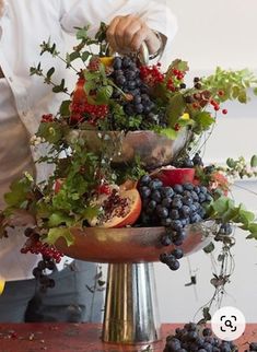 a man standing in front of a metal bowl filled with fruit and veggies